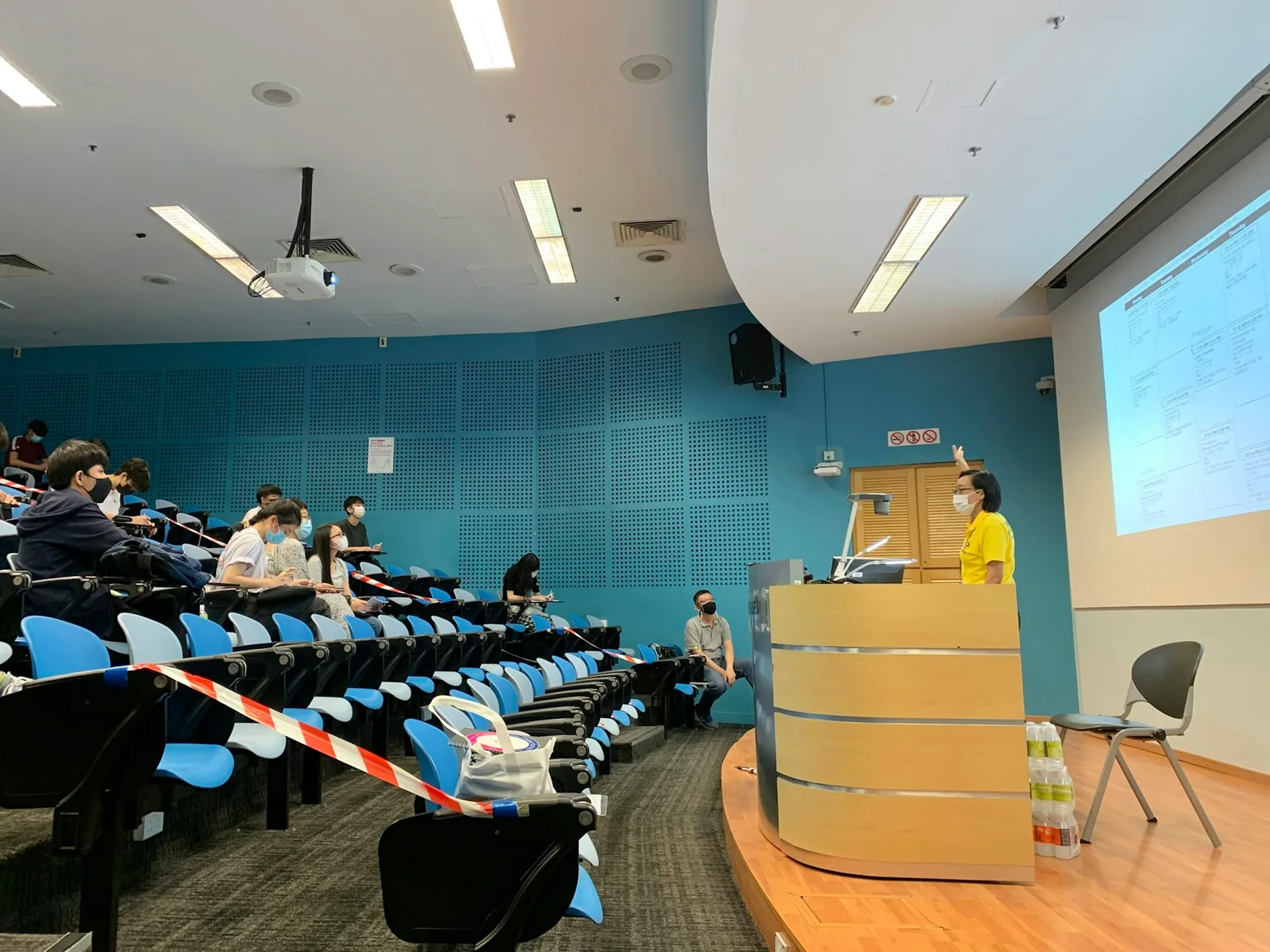 An audience facing a lectern and projection screen in a lecture room